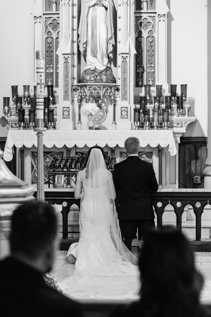 Black and white photo of a bride and groom praying during their St. John the Evangelist Catholic Church wedding ceremony in Indianapolis, Indiana