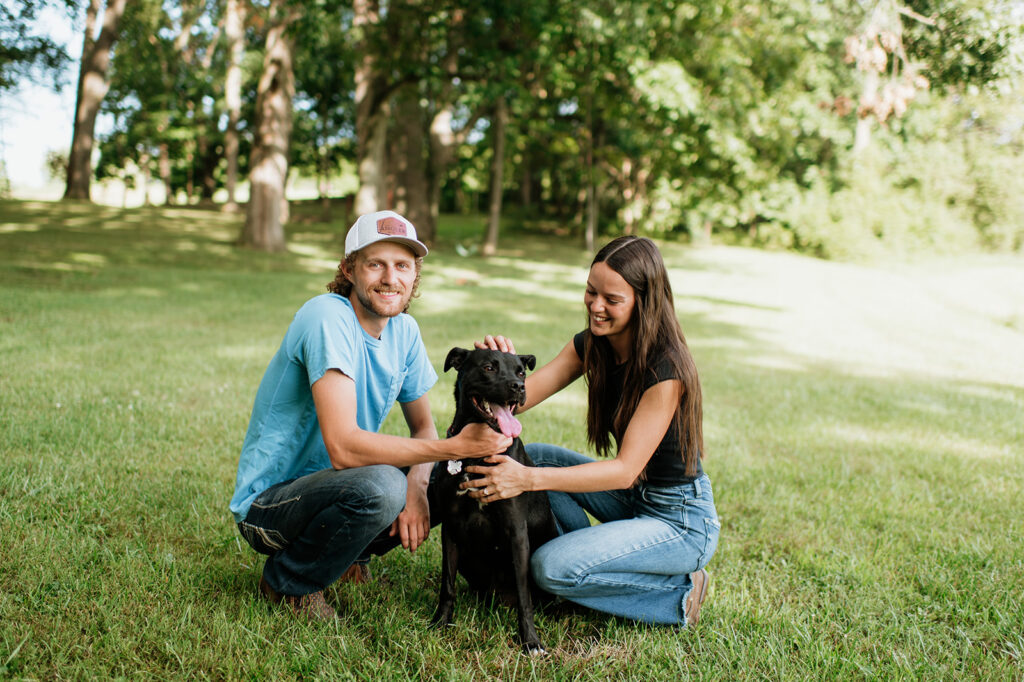 Couple sitting in the grass with their dog