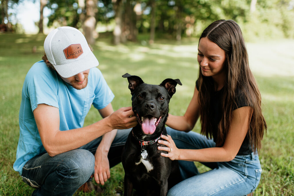 Couple sitting in the grass and petting their dog