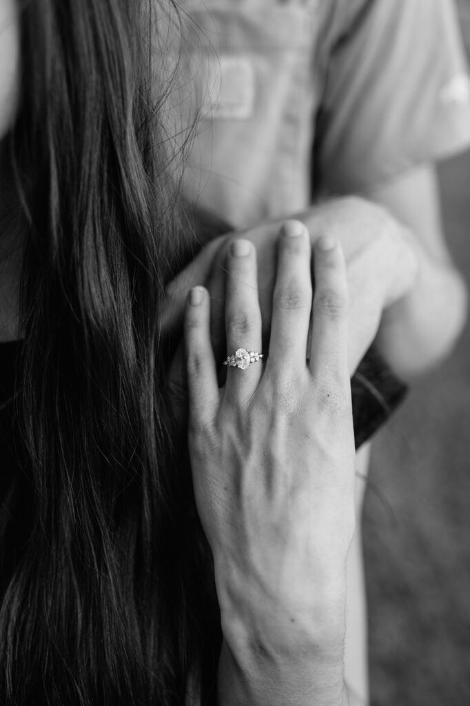 Close up black and white photo of a woman showing off her three-stoned engagement ring