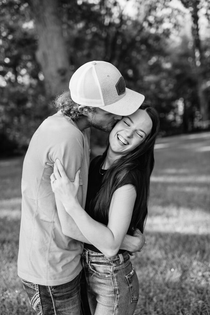 Black and white photo of a man kissing his fiancé on the cheek