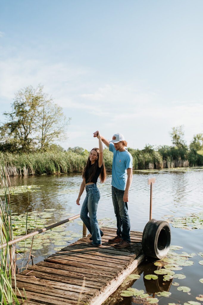 Man twirling his fiancé as they stand on a deck over a pond for their Midwest engagement photos in Albion, Indiana