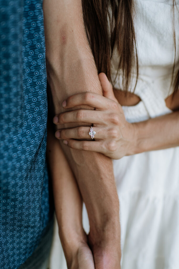 Close up shot of a woman holding her fiancés arm and showing off her engagement ring