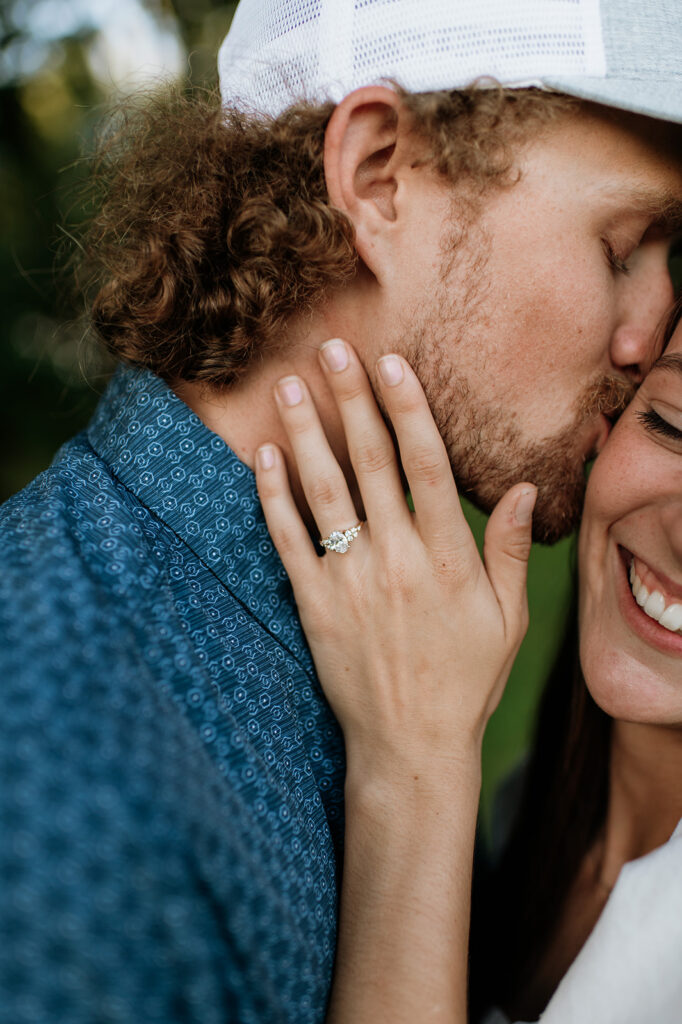 Close up photo of a man kissing his fiancé as she smiles