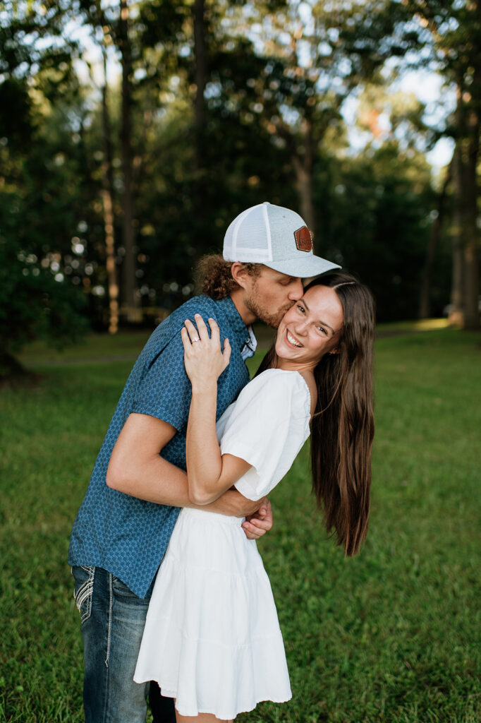 Man kissing his fiancé on the cheek as she smiles