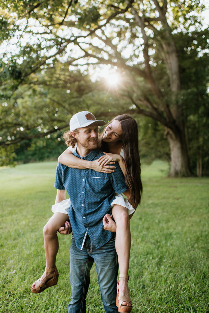 Man giving his fiancé a piggy back ride during their woodsy Midwest engagement photos in Albion, Indiana