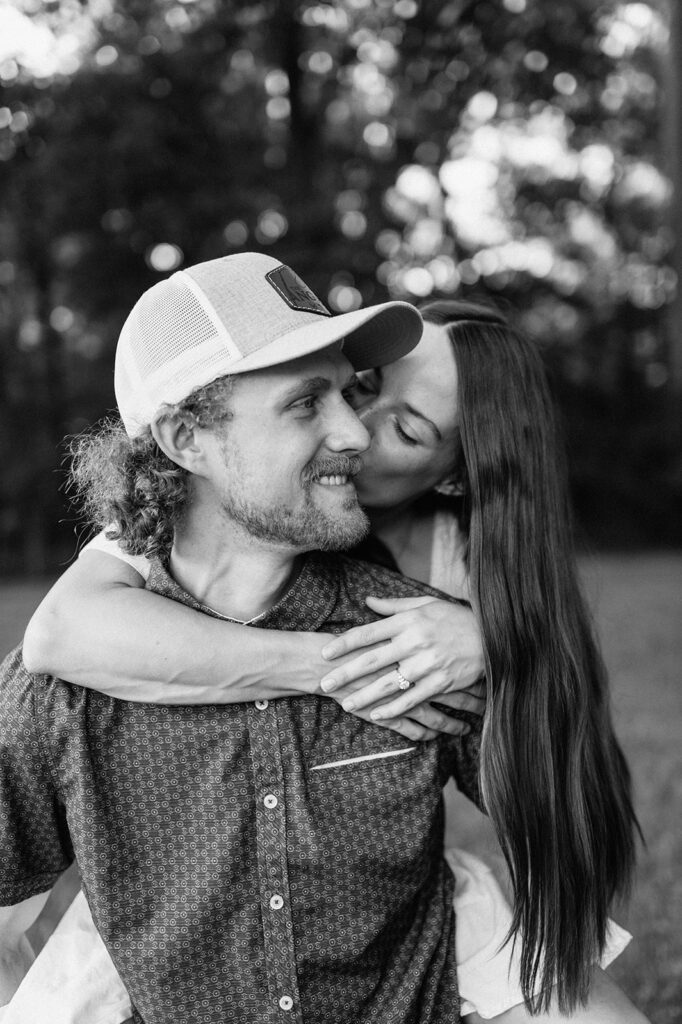 Black and white photo of a woman kissing her fiancé on the cheek