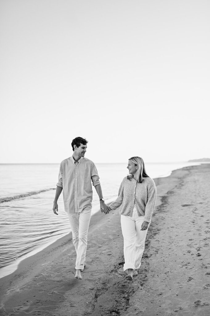 Black and white photo of a man and woman walking on Gordon Beach after their surprise proposal in Michigan