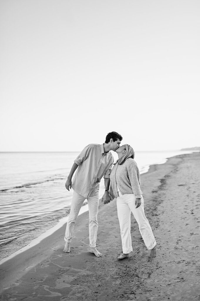 Black and white engagement photo of a couple kissing on Gordon Beach after their surprise proposal in Michigan