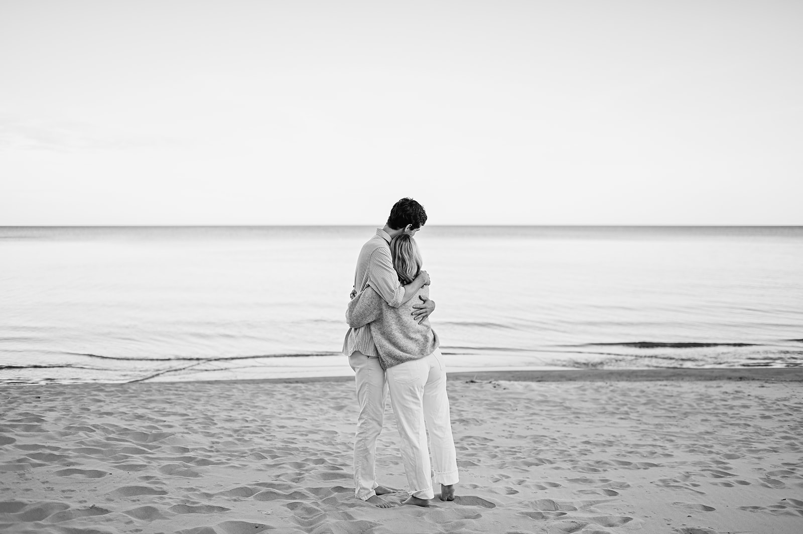 Black and white photo of a man and woman hugging after their Michigan surprise proposal on Gordon Beach