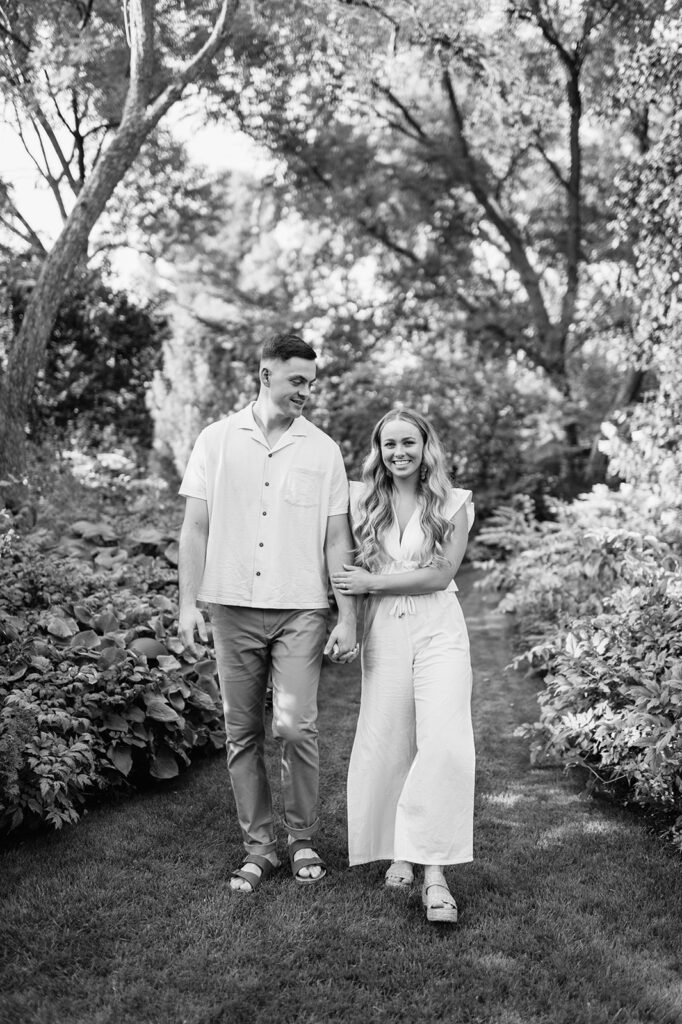 Black and white engagement photo of a couple walking through Hamstra Gardens in Wheatfield, Indiana for their engagement session