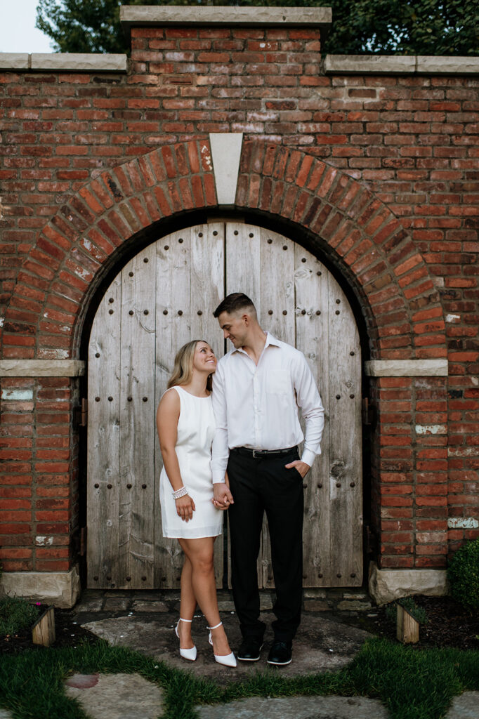 Couple smiling at each other as they pose for their engagement photos at Hamstra Gardens