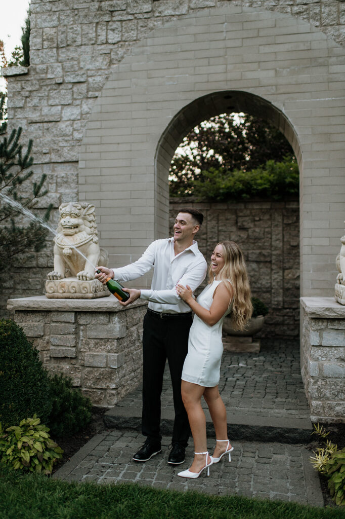 Couple popping champagne together at Hamstra Gardens in Wheatfield, Indiana during their engagement session