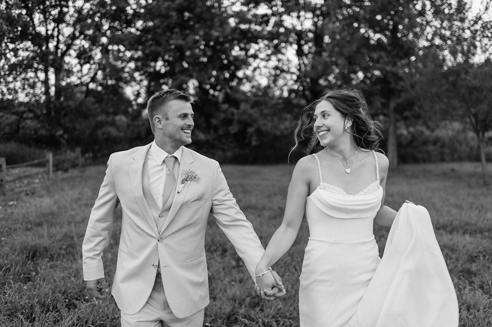 Black and white photo of a bride and groom running in an open field