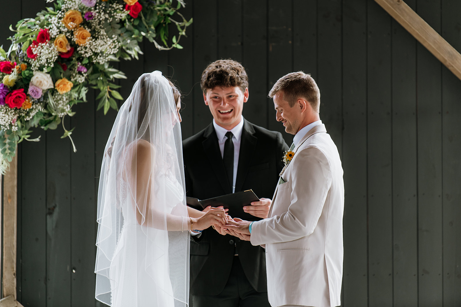 Bride and groom exchanging rings during their outdoor Empeiria 110 wedding ceremony underneath the pavilion 