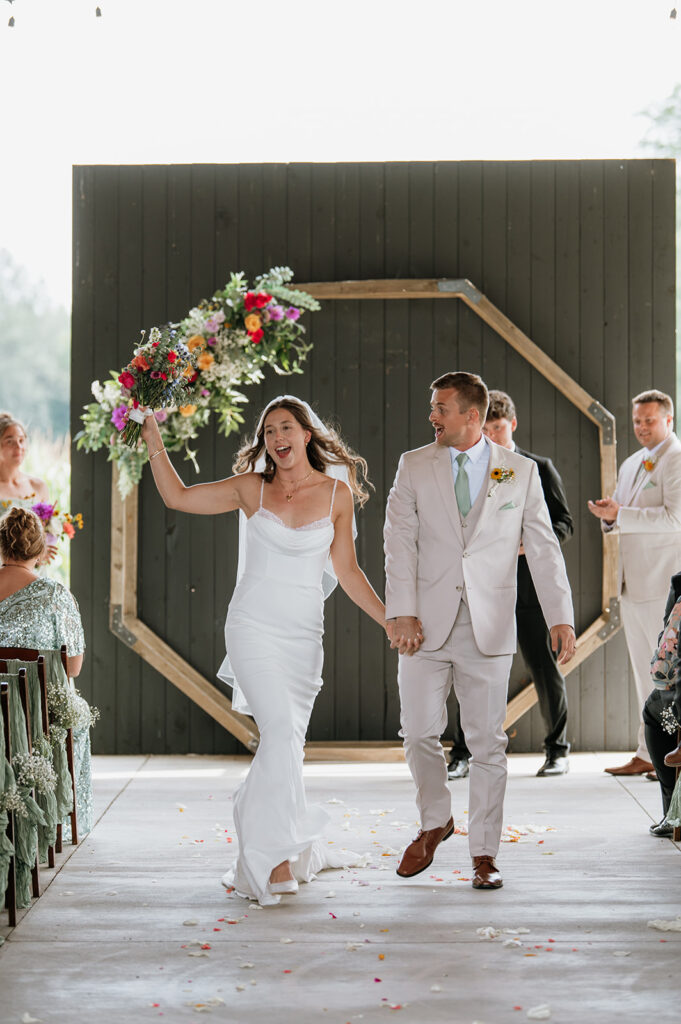 Bride and groom walking back down the aisle as husband and wife during their outdoor Empeiria 110 wedding ceremony underneath the pavilion 