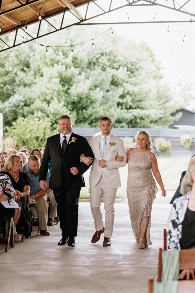 Groom being walked down the aisle by his parents