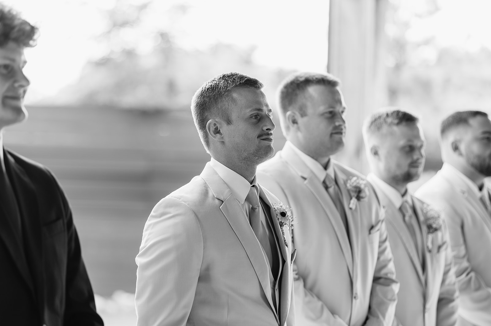 Black and white photo of a groom seeing his bride walk down the aisle