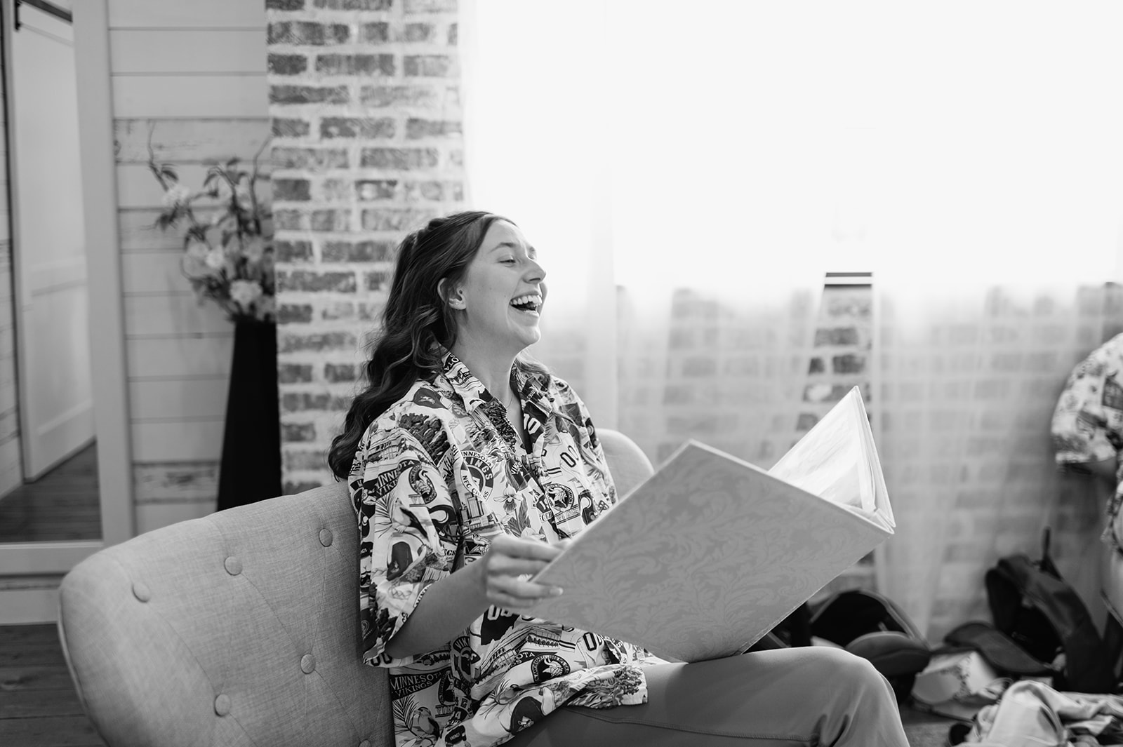 Black and white photo of a bride laughing at a scrapbook from her bridesmaids