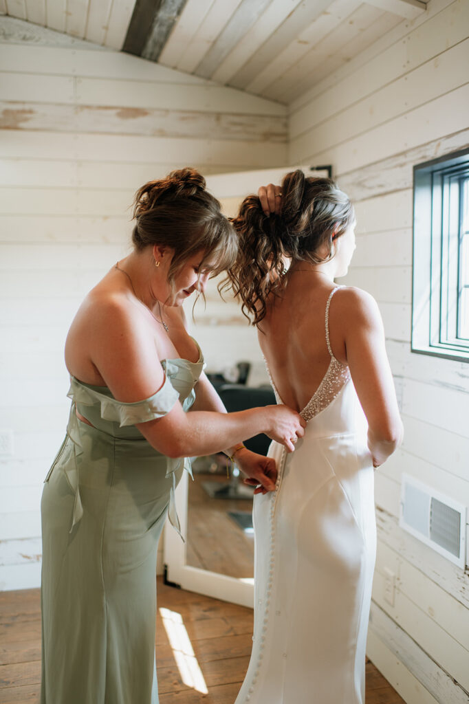 Bridesmaid helping bride get her wedding dress zipped up