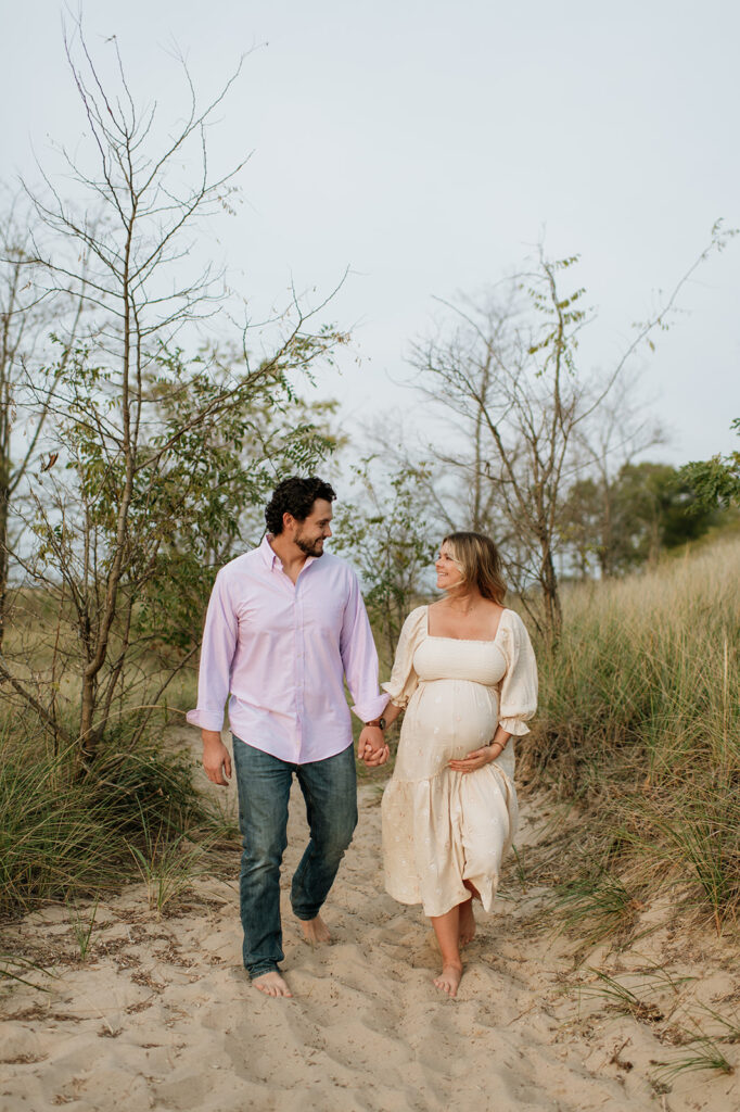 Couple holding hands and walking the beach path for their maternity photos in Michigan at New Buffalo beach