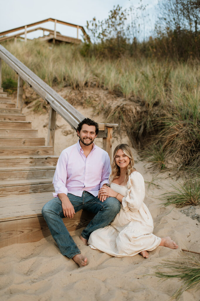 Couple sitting by beach stairs for their maternity photos in Michigan