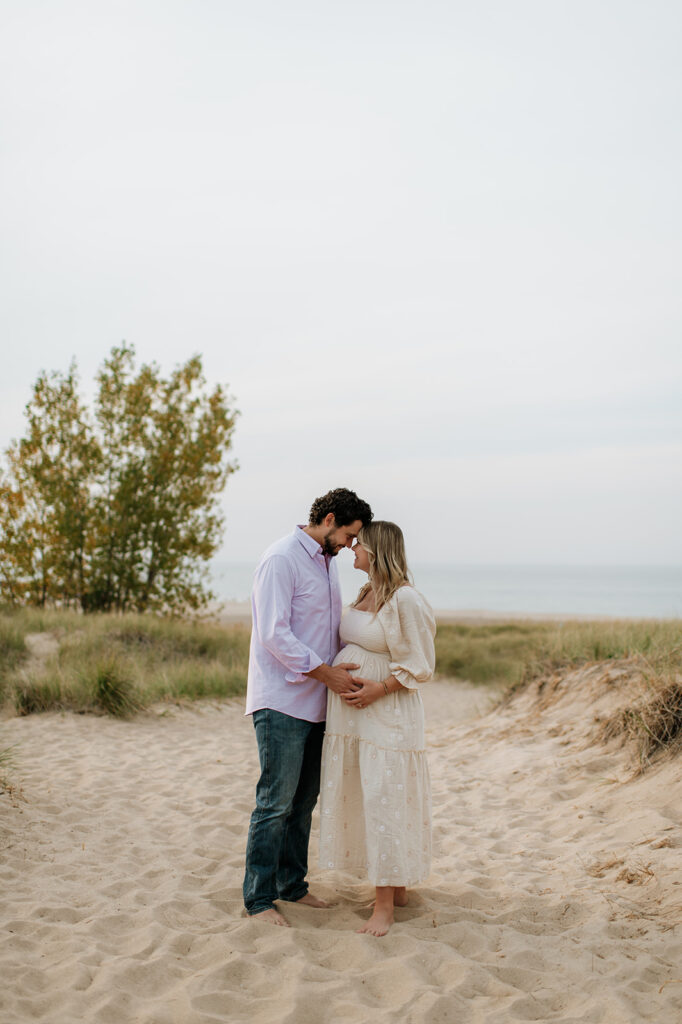 Man and woman touching noses during their beach maternity shoot