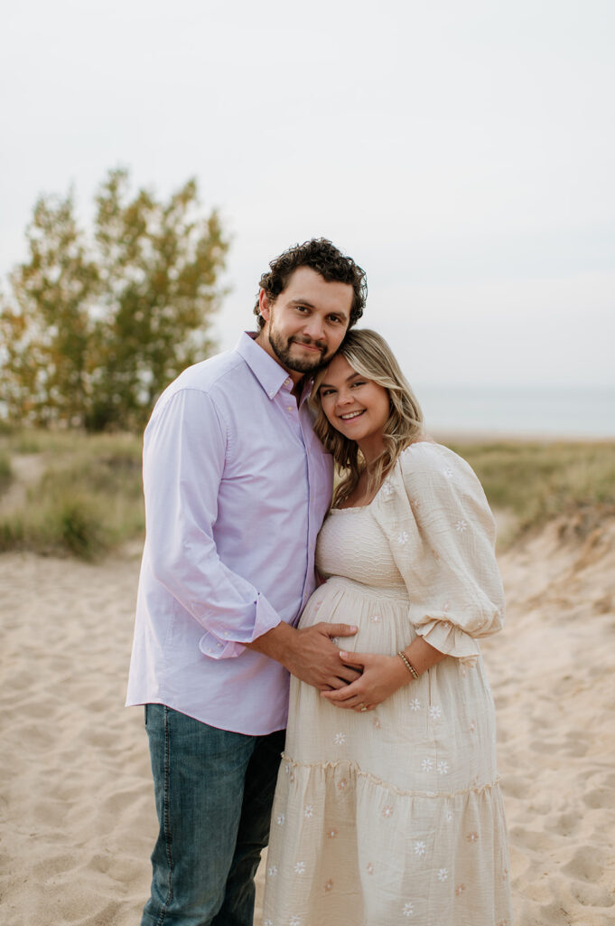 Man holding his wifes pregnant belly during their Michigan beach maternity session