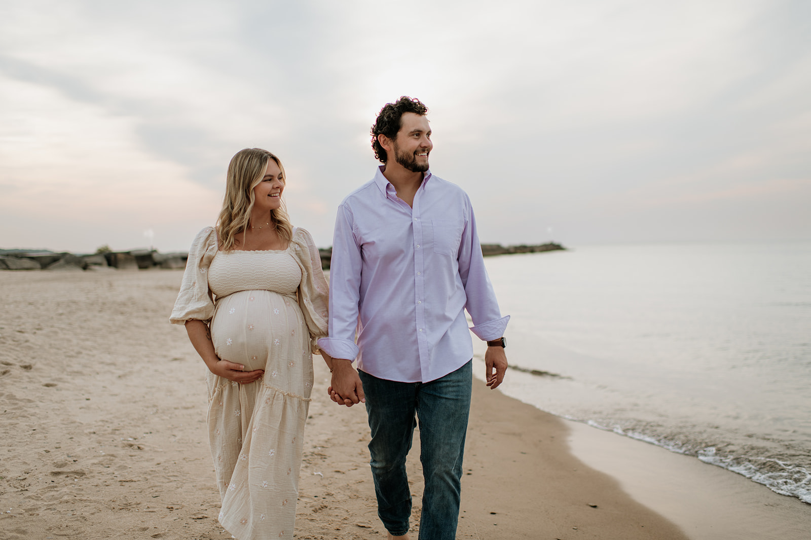 Man and woman walking the coastline of New Buffalo Beach for their Michigan maternity photos