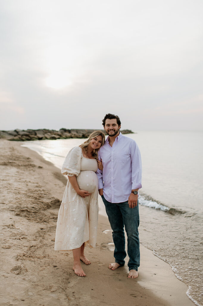 Couple posing next to the water for their Michigan beach maternity photos