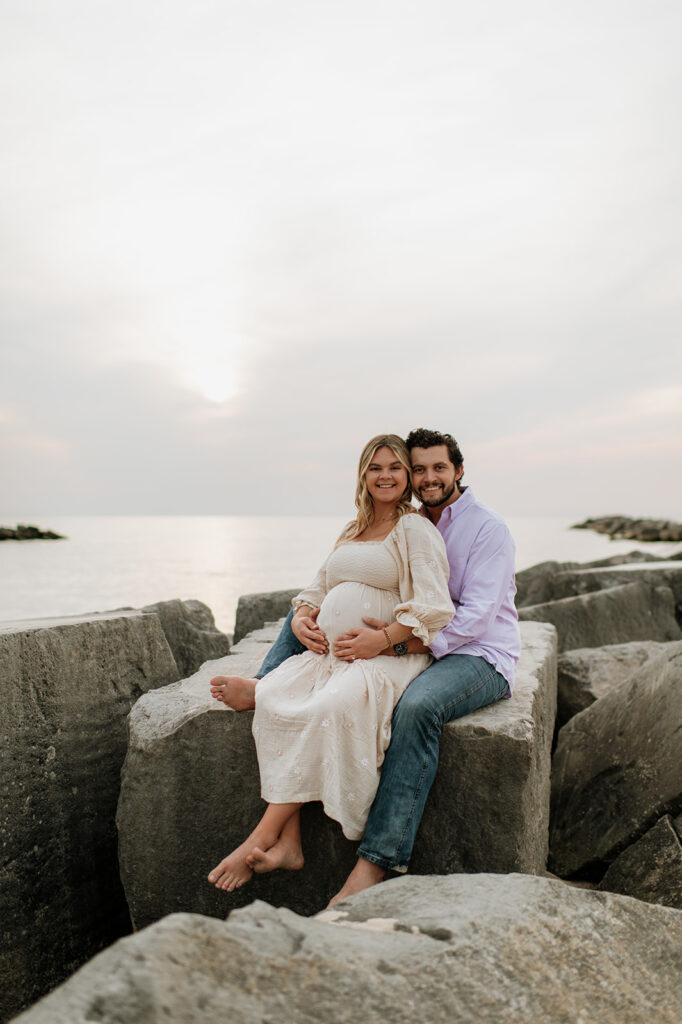 Couple sitting on beach rocks for their maternity session