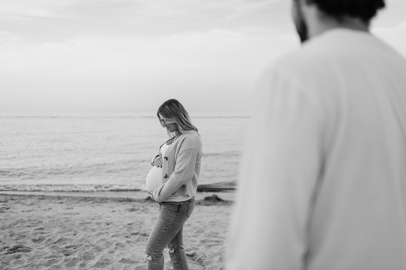 Black and white photo of a man admiring his pregnant wife on the beach