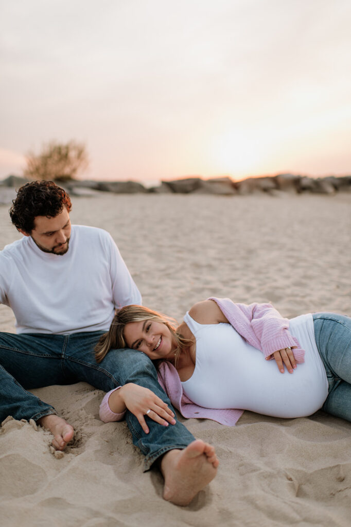 Pregnant woman laying on her husbands lap during their beach maternity session