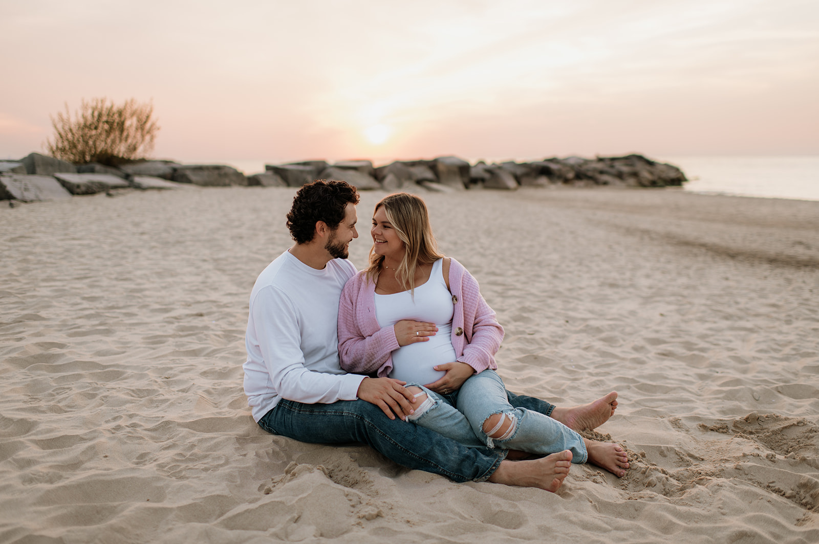 Man and woman laying on the beach during their couples Michigan maternity photos at sunset