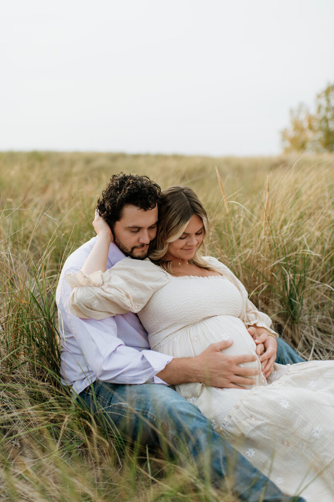 Couple posing in beach grass at New Buffalo Beach for their dreamy maternity photos in Michigan