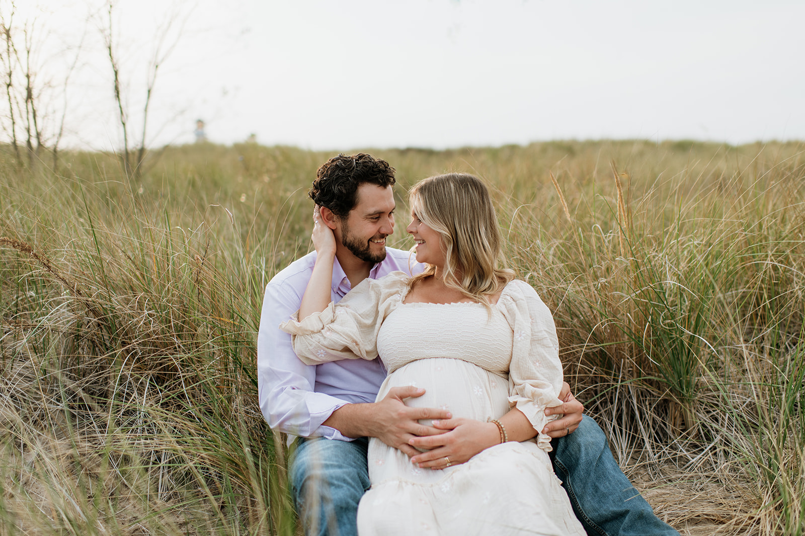 Man and woman sitting in beach grass at New Buffalo Beach for their maternity photos in Michigan