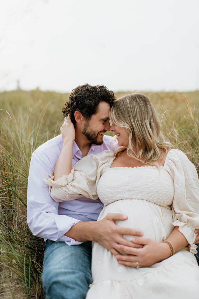 Man and woman sitting in beach grass at New Buffalo Beach for their maternity photos in Michigan