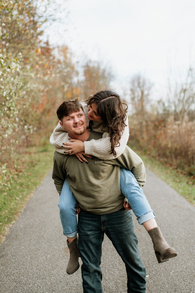 Man giving his fiancé a piggy back ride during their Northern Indiana engagement photos at Potato Creek State Park