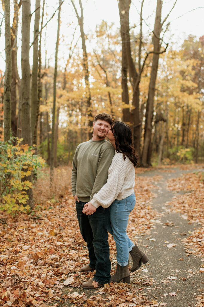 Woman kissing her fiancé on the cheek during their fall engagement session