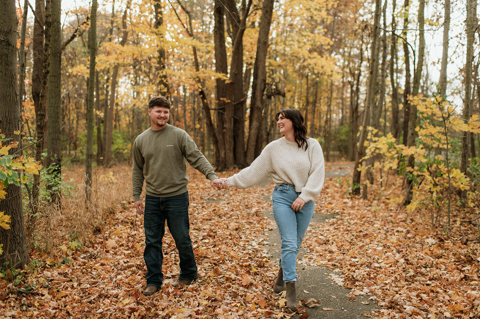 Man and woman holding hands and walking through Potato Creek State Park during their Northern Indiana engagement photos