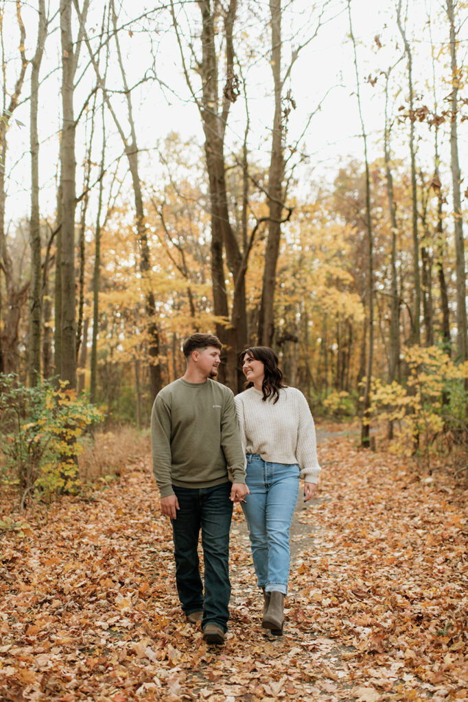 Man and woman holding hands and walking through Potato Creek State Park during their Northern Indiana engagement photos