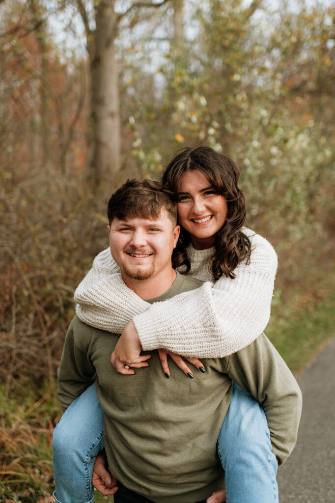 Man giving his fiancé a piggy back ride during their Northern Indiana engagement photos at Potato Creek State Park