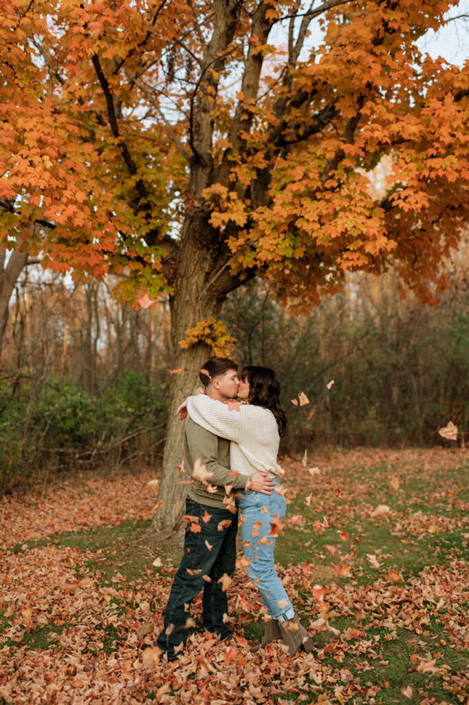 Couples fall engagement photos underneath a tree with leaves falling down