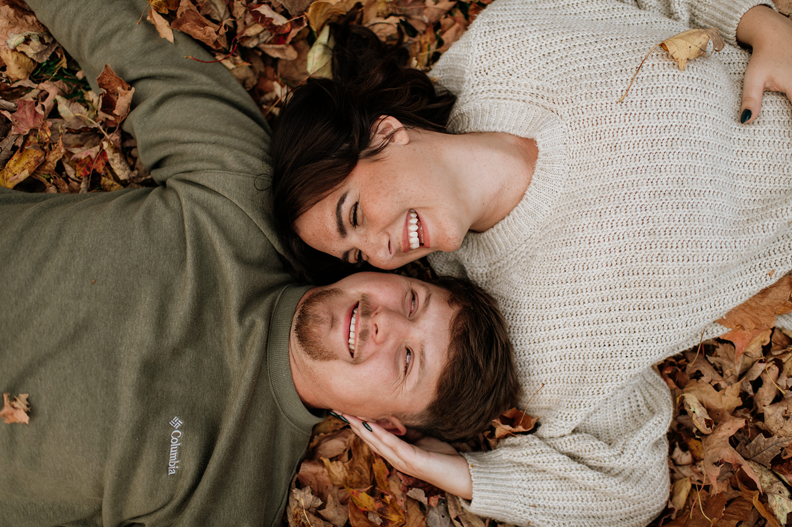 Couple laying in fallen leaves fur their fall Northern Indiana engagement photos at Potato Creek State Park