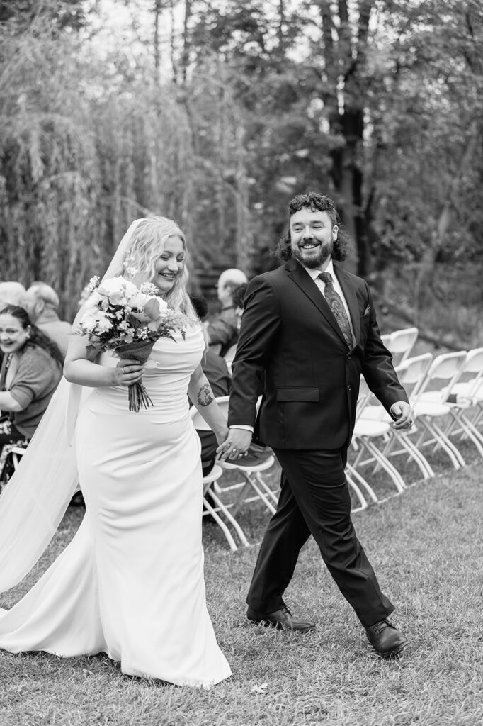 Black and white photo of a bride and groom walking back down the aisle as husband and wife