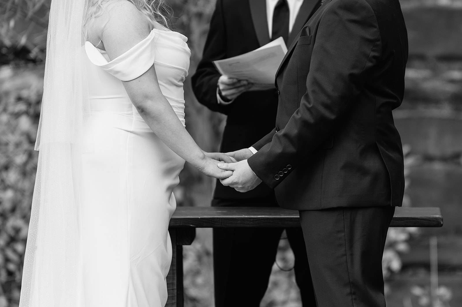 Black and white photo of a bride and groom holding hands during their ceremony