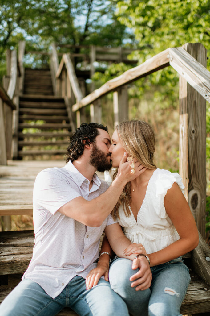 Couple sitting on a set of stairs and kissing during their outdoor summer engagement photos