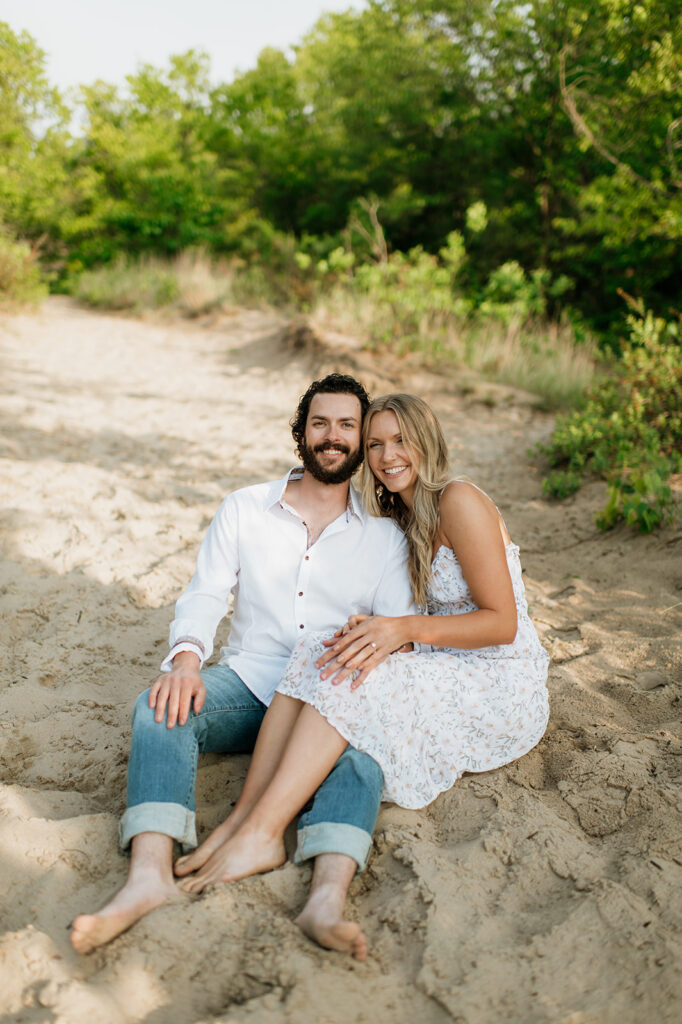 Couple sitting in the sand for their summer beach engagement session