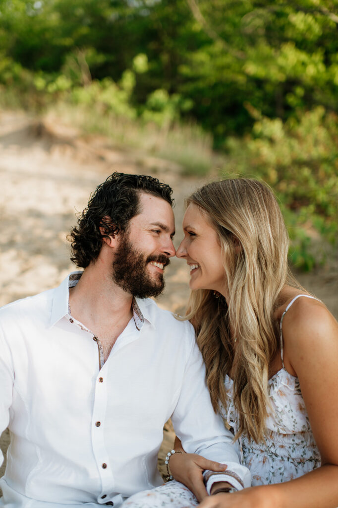 Couple sitting in the sand for their summer beach engagement session