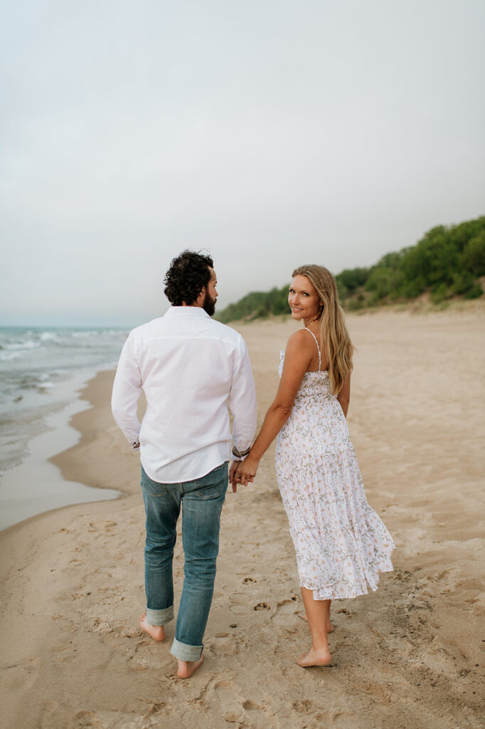 Couple walking along the shoreline at Indiana Dunes National Park for their beach engagement photos